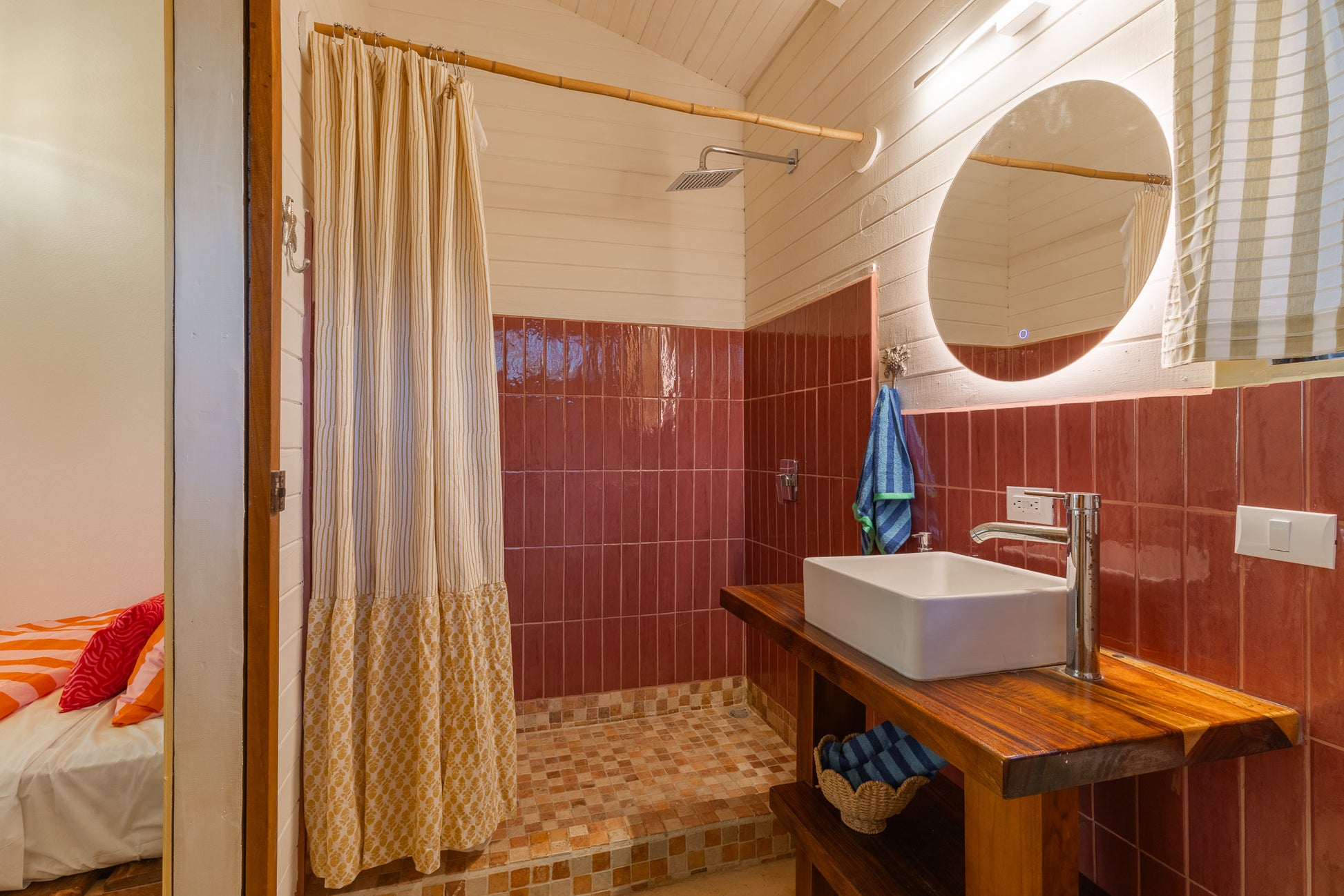 Studio Mango — Bathroom with red tiles, round lit mirror and wooden vanity