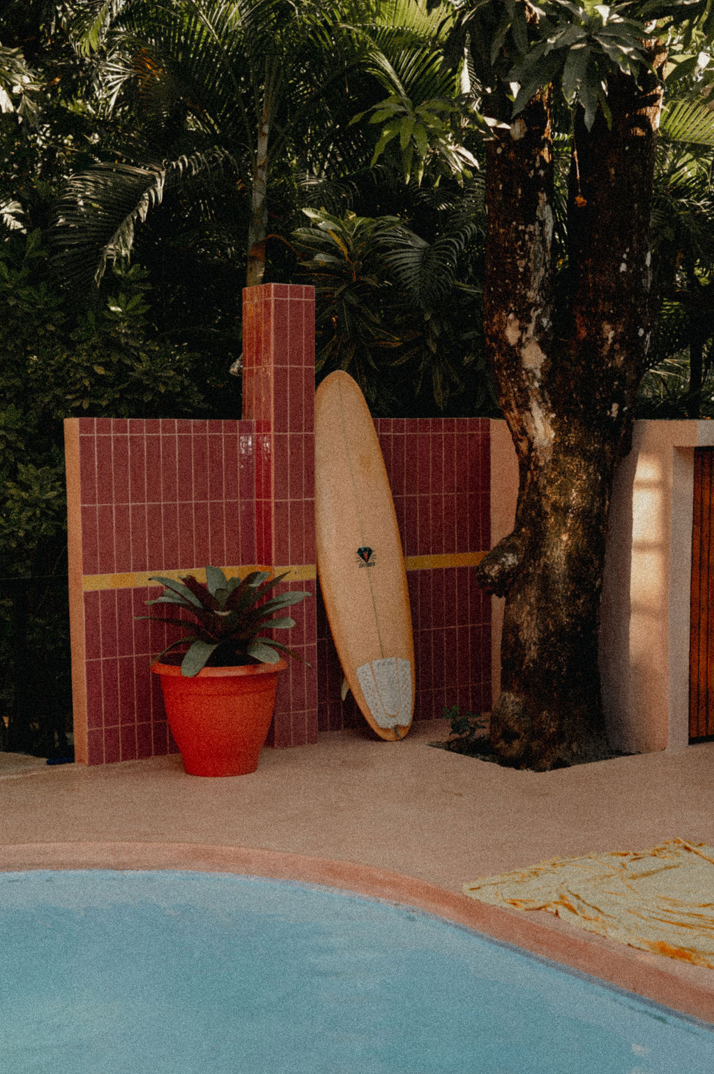 Surfboard leaning against pink tile by the pool