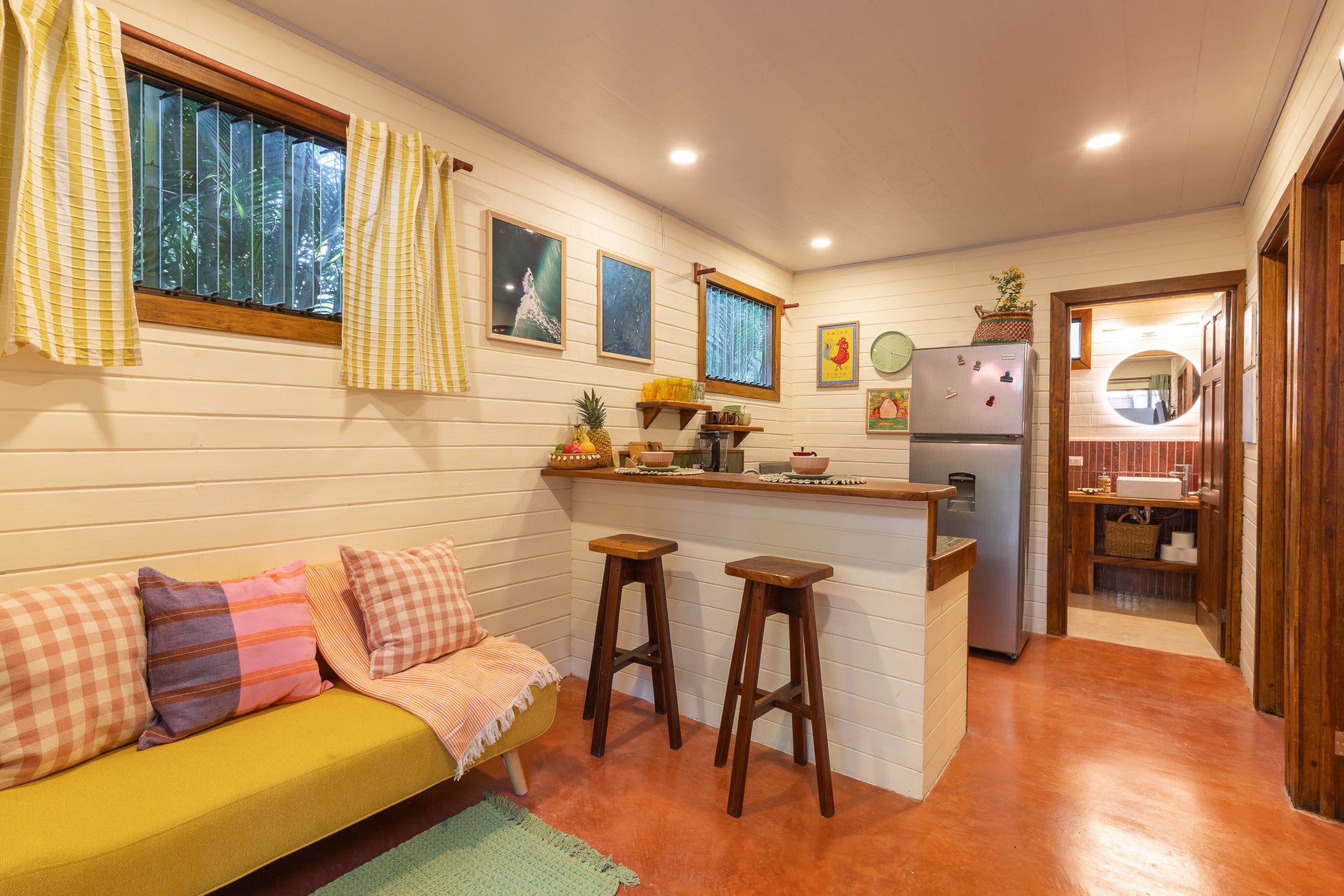 Apartment Papaya — Living area with yellow sofa, breakfast bar with two stools, and fridge