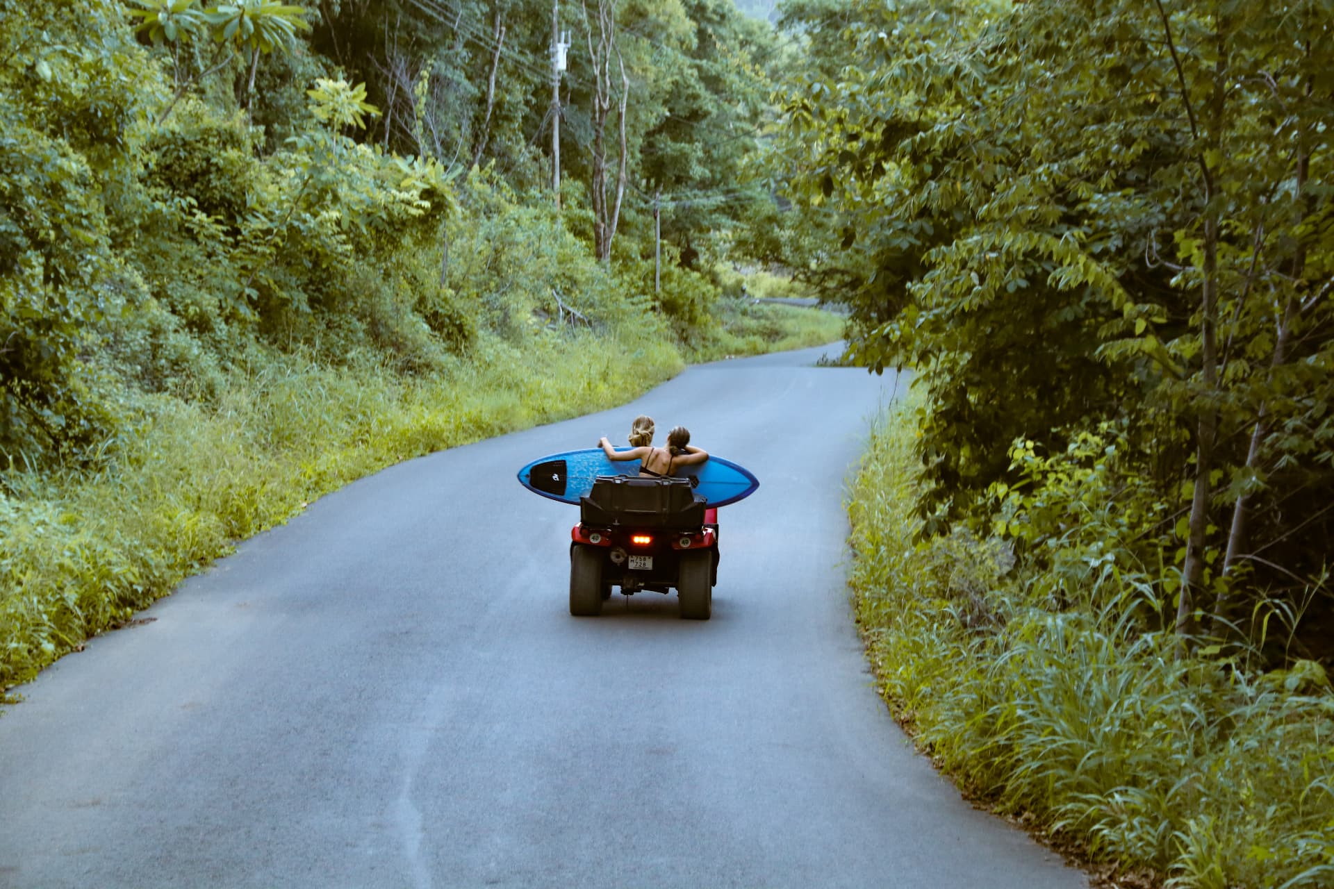 Riding an ATV down a jungle road with a surfboard on the back