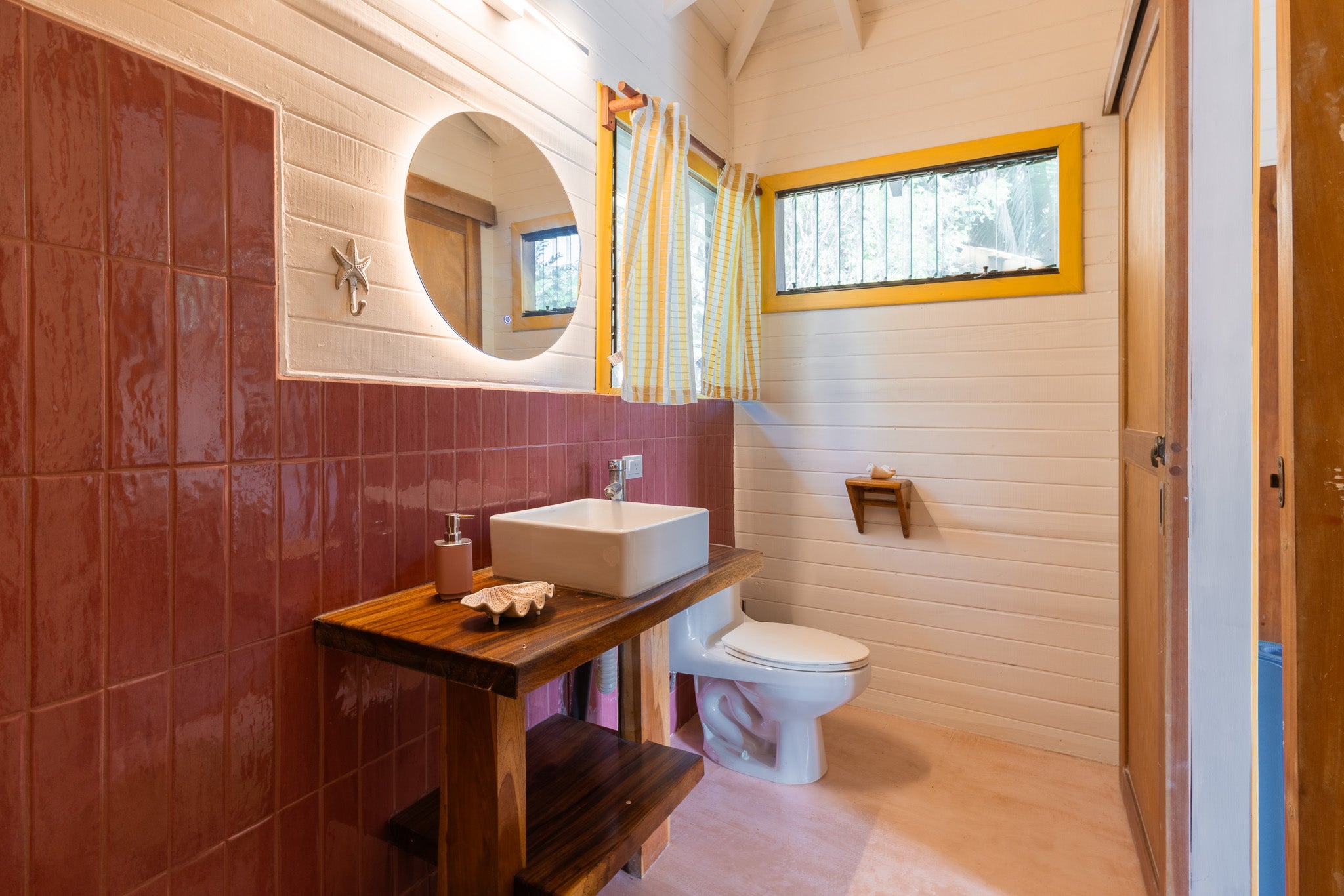 Studio Limón — Bathroom with red tiles, round lit mirror and wooden vanity
