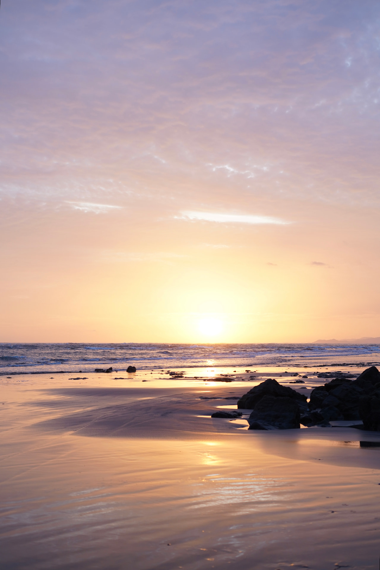Soft pink sunset over rocks and wet sand