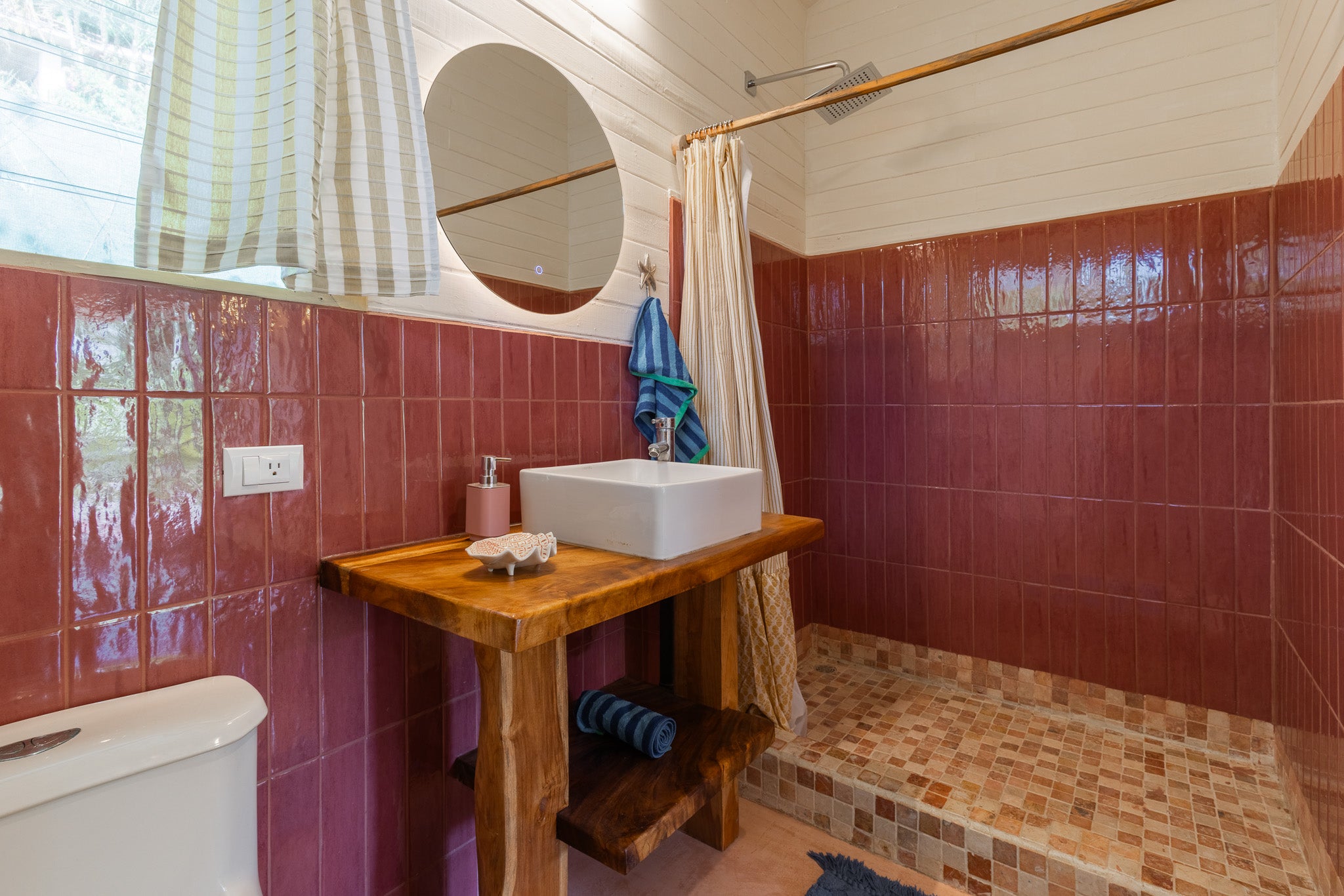 Studio Coco — Bathroom with red tiles, round lit mirror and wooden vanity